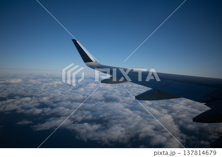 飛行機の窓から望む、青空と広大な雲海を飛ぶ航空機の翼 137814679