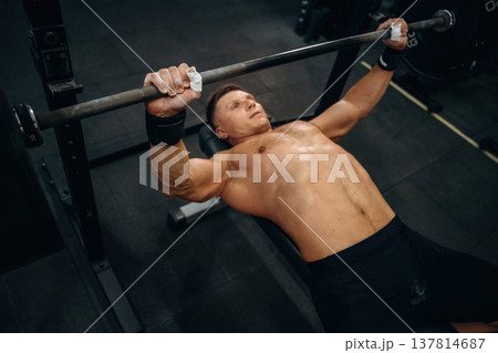 Lying down and pushing the barbell. Athletic man performing weightlifting exercises in a gym Lying down and pushing the barbell. Athletic man performing weightlifting exercises in a gym 137814687