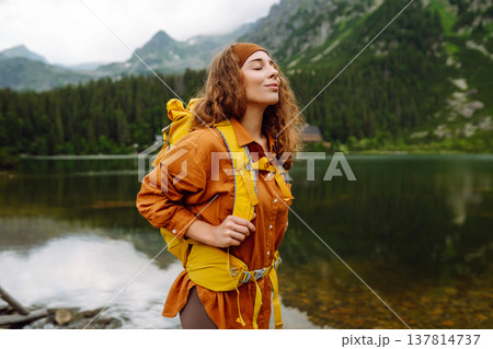 Travel Slovakia, Europe. Tourist with a yellow backpack stands against the backdrop of alpine lake. Travel Slovakia, Europe. Tourist with a yellow backpack stands against the backdrop of alpine lake. 137814737
