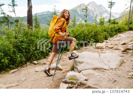Young woman traveler hiking poles on trail among the mountains. Hiking. Active lifestyle. Young woman traveler hiking poles on trail among the mountains. Hiking. Active lifestyle. 137814743
