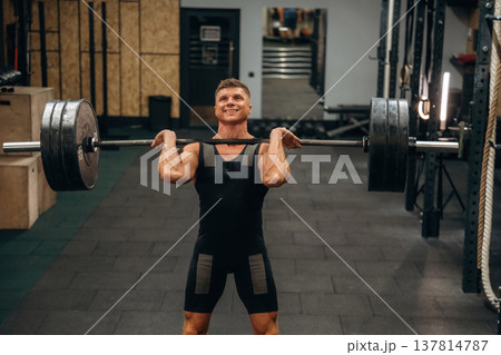 Strong arms and back. Athletic man performing weightlifting exercises with a barbell in a gym 137814787