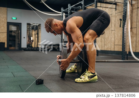 Adding more weight. Athletic man performing weightlifting exercises with a barbell in a gym Adding more weight. Athletic man performing weightlifting exercises with a barbell in a gym 137814806