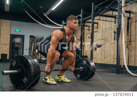 Ready for lifting. Athletic man performing weightlifting exercises with a barbell in a gym 137814811