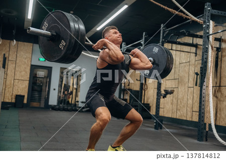 Conception of weightlifting. Athletic man is doing exercise with a barbell in a gym 137814812