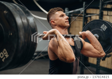 Conception of weightlifting. Athletic man is doing exercise with a barbell in a gym 137814815