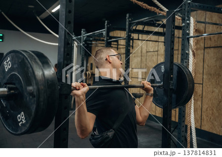 Funny man in glasses is trying to lift the heavy barbell in the gym 137814831
