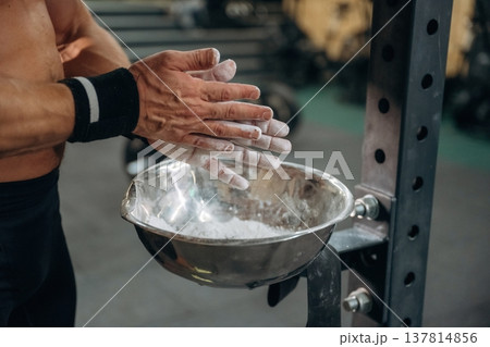 Fitness man is rubbing his hands with chalk, specifically magnesium carbonate 137814856