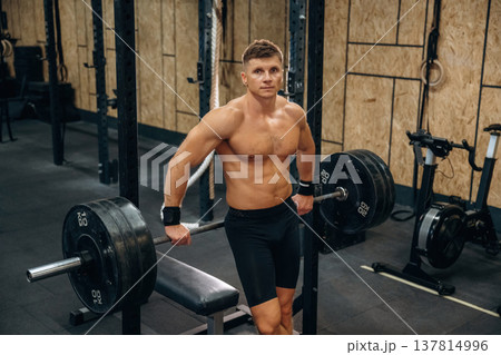 Break, posing. Athletic man performing weightlifting exercises with a barbell in a gym 137814996