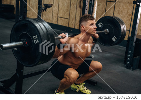 Sitting, ready for squats. Athletic man performing weightlifting exercises with a barbell in a gym 137815010