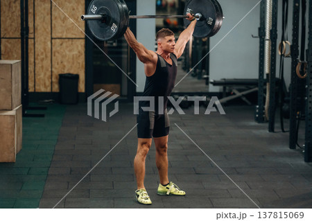 Side view. Athletic man performing weightlifting exercises with a barbell in a gym 137815069