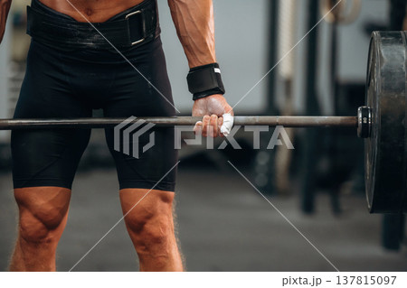 Hands are in white powder. Close up view of athletic man that is lifting heavy barbell 137815097