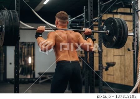 Barbell is on the neck and in hands. Athletic man performing weightlifting exercises in a gym 137815105
