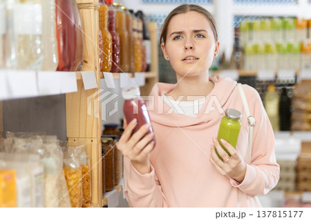 Girl customer in supermarket examines smoothie, chooses food-stuff in health lifestyle store 137815177