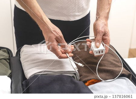 Charging cables and clothes inside open suitcase, Hands hold charger, wire above packed clothes in Charging cables and clothes inside open suitcase, Hands hold charger, wire above packed clothes in 137816061