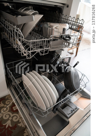 Dishwasher racks holding a full load of dirty dishes, including plates, pots, pans, and cutlery, ready for a cleaning cycle in a contemporary kitchen setting Dishwasher racks holding a full load of dirty dishes, including plates, pots, pans, and cutlery, ready for a cleaning cycle in a contemporary kitchen setting 137816268