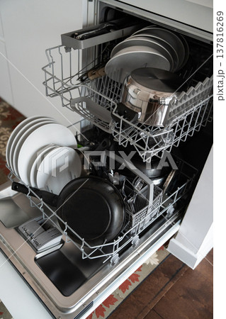 Open dishwasher loaded with dirty dishes, plates, bowls, and cutlery, ready for washing, showing the domestic task of everyday kitchen cleaning 137816269