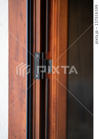 Black metal door hinge attaching a dark wooden frame to a white wall, providing security and functionality for residential or commercial buildings 137816399