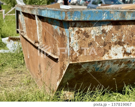 An Old and Rusty Dump Container That is Surrounded by Lush, Overgrown Grass and Weeds. A weathered metal dumpster overflowing with various debris, positioned against a backdrop of lush tall grass. 137819067