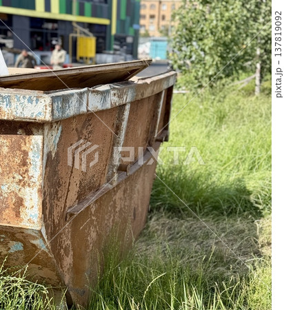 An Old and Rusty Dump Container That is Surrounded by Lush, Overgrown Grass and Weeds. A weathered metal dumpster overflowing with various debris, positioned against a backdrop of lush tall grass. 137819092