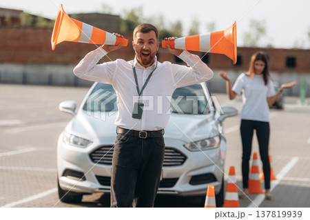 Fun by using cones. Man instructor in the driving school and woman are outside the car Fun by using cones. Man instructor in the driving school and woman are outside the car 137819939