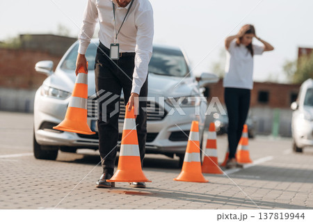 Placing the guide cones. Man instructor in the driving school and woman are outside the car 137819944
