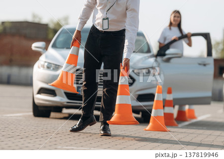 Placing the guide cones. Man instructor in the driving school and woman are outside the car Placing the guide cones. Man instructor in the driving school and woman are outside the car 137819946