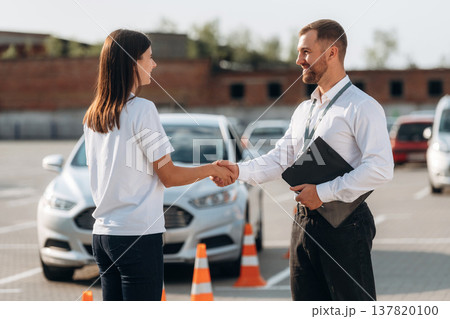 Shaking hands. Man instructor in the driving school and woman are outside the car Shaking hands. Man instructor in the driving school and woman are outside the car 137820100