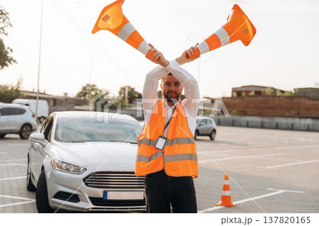 Wellness conception, having fun with the cones. The road worker in orange uniform is with cones near car 137820165