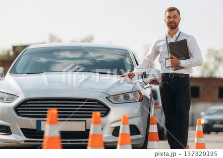 Leaning on the car. Driving school worker is outdoors 137820195