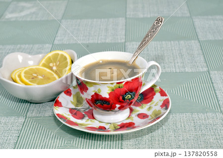 There is a cup of tea and a dish with lemon on the table. 137820558