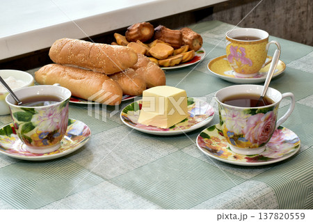 There are cups of tea and a plate of bread on the table. 137820559