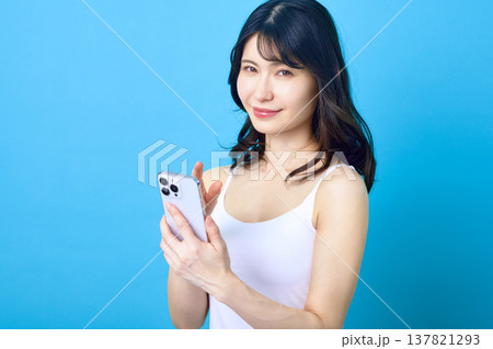 スマートフォンを操作して微笑む若い日本人女性 青背景 137821293