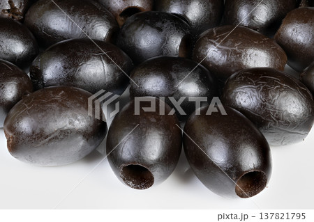 Olives on platter. Black olives with pits showcased. Closeup of moist black olives on white background. Arrangement of shiny black olives with pits on clean white surface 137821795