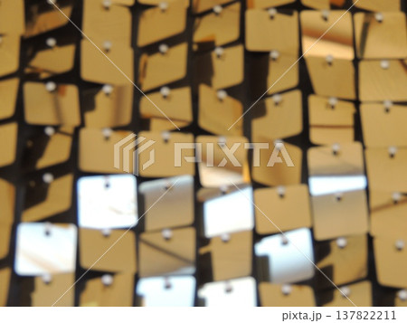 Shiny plastic golden squares suspended on strings as interior decor elements, holiday decorations in gold style with shimmering surface and geometric details in blurred focus 137822211