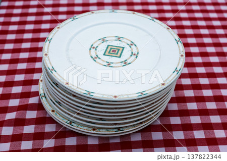Stack of pristine, beautiful plates arranged on a checkered tablecloth, showcasing elegance and simplicity in a cozy dining setting, perfect for any occasion 137822344