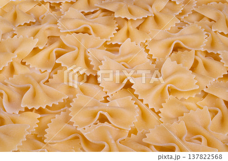 Farfalle shapes create textured design. beige pasta texture with detailed edges. Repetitive bowshaped pasta silhouettes form uniform pattern background 137822568