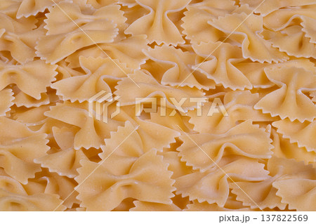 Closeup of rustic dry pasta. Artisan bowtie pasta with textured edges. Detailed macro image of golden uncooked farfalle pasta highlighting textured ruffled borders 137822569