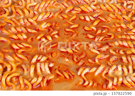 Close shot of flavorful broth and spiraled noodles showcasing texture. Detailed view of glossy orange broth surrounding spiral noodles with spice flecks and comforting warmth Close shot of flavorful broth and spiraled noodles showcasing texture. Detailed view of glossy orange broth surrounding spiral noodles with spice flecks and comforting warmth 137822590