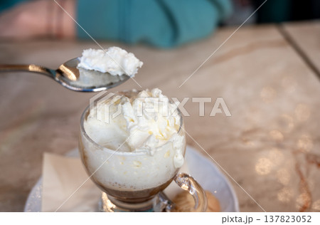 Milan, italy, april 1, 2024. Person enjoying a coffee drink topped with sweet whipped cream, using a spoon for dessert while having breakfast in a cafe Milan, italy, april 1, 2024. Person enjoying a coffee drink topped with sweet whipped cream, using a spoon for dessert while having breakfast in a cafe 137823052