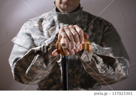 Soldier in camouflage uniform holding a cane, symbolizing veteran support and resilience Soldier in camouflage uniform holding a cane, symbolizing veteran support and resilience 137823301