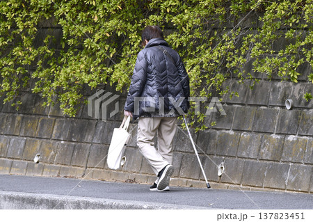 日本の横浜都市景観枝が…下を向いて歩道を歩く杖の高齢女性(マスク姿)、…人生とは…＝横浜市内 137823451