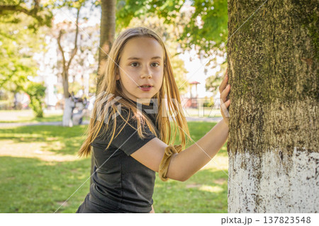 Playful little girl with long brown hair standing on summer nature park outdoors. Kid's portrait Playful little girl with long brown hair standing on summer nature park outdoors. Kid's portrait 137823548