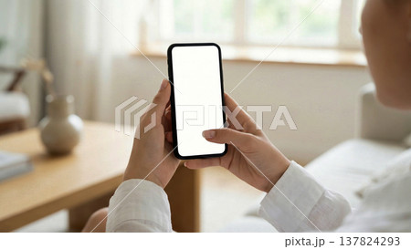 白い画面のスマートフォンを操作する女性の手元のモックアップ素材 137824293