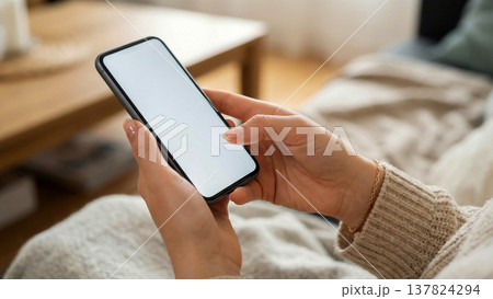 白い画面のスマートフォンを操作する女性の手元のモックアップ素材 137824294