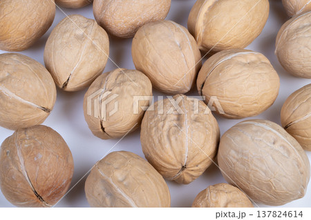 Closeup cluster of walnuts in shells on white backdrop, natural brown tones, shallow depth of field, rough shell texture, food styling for snack and ingredient photography 137824614