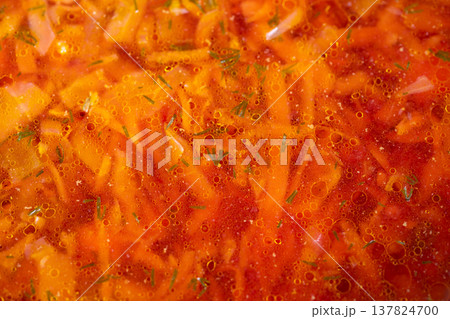 Hearty homemade soup. Comforting rustic borscht with potatoes and shimmering fat beads. Homemade beet and cabbage soup simmering in aged cast iron pot under warm kitchen light 137824700