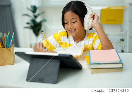 Asian girl with headphones enjoying online class on digital tablet Asian girl with headphones enjoying online class on digital tablet 137824850