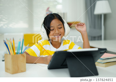 Asian girl with headphones enjoying online class on digital tablet Asian girl with headphones enjoying online class on digital tablet 137824851