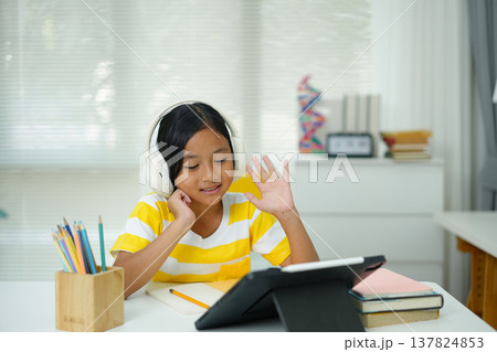 Young student waving during online class while using tablet for remote learning at home desk Young student waving during online class while using tablet for remote learning at home desk 137824853