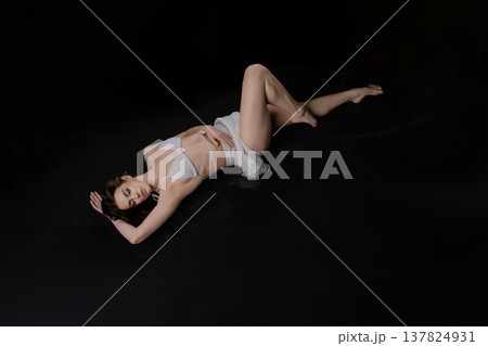 Elegant woman in white lingerie lying on a black reflective surface with copy space. Elegant woman in white lingerie lying on a black reflective surface with copy space. 137824931